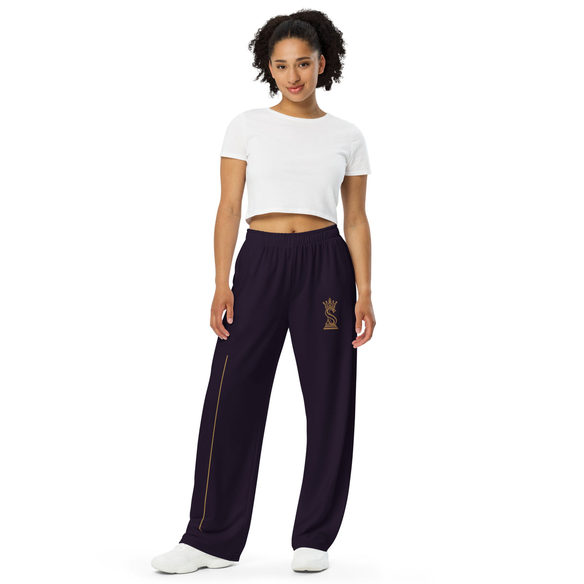 Model wearing black wide-leg pants with gold crowned-S queen emblem on the thigh, front view