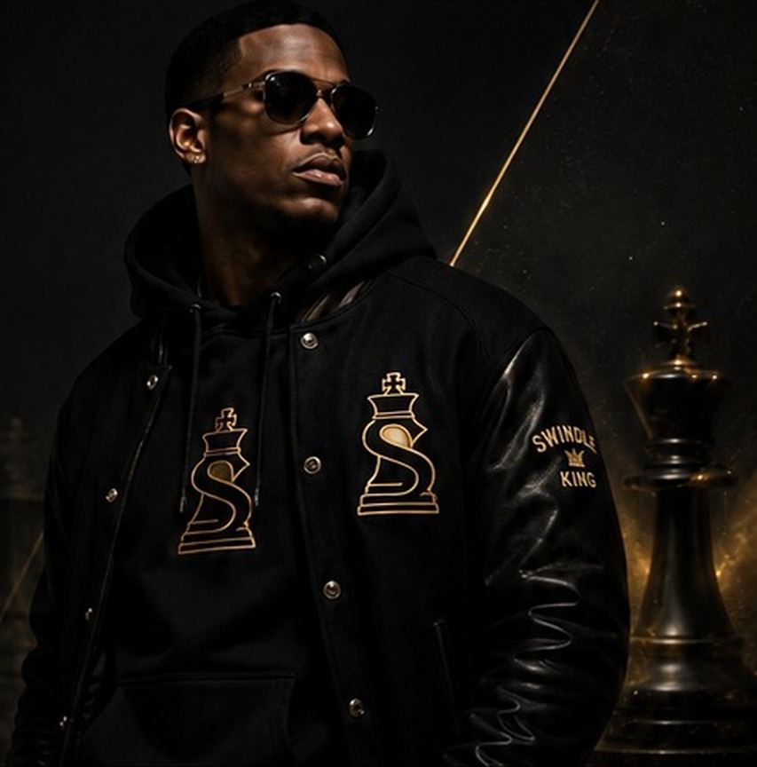 Model in the black Swindle King varsity jacket and Signature hoodie beside a gold-lit chess king